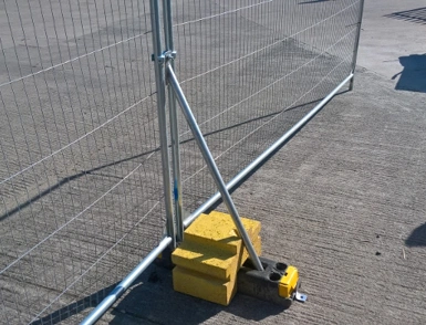 Temporary mesh construction fence panel secured with bracing and ballast blocks on pavement