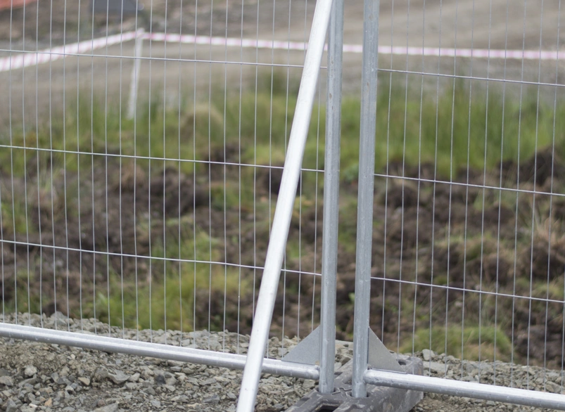 Temporary construction fence panel with stabiliser brace and weighted base on gravel