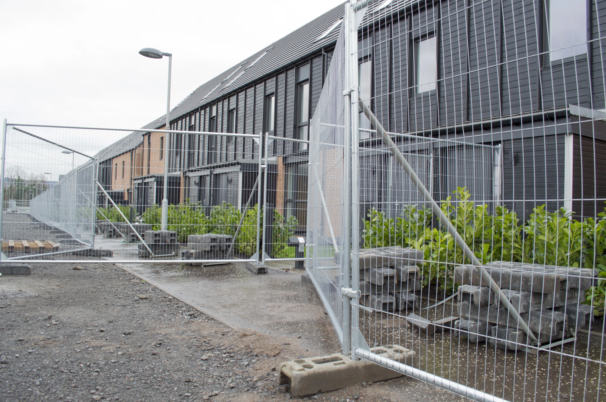 Anti-climb fence panels securing a construction site walkway outside new-build houses.