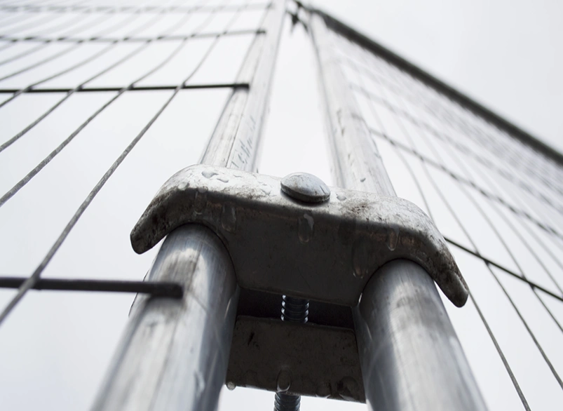 Close-up of galvanised temporary construction fence post coupler and wire mesh panel