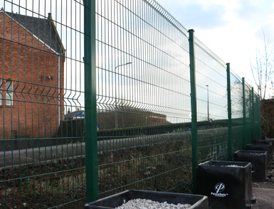Green welded mesh security fence line with FenceSafe ballast blocks along a roadside