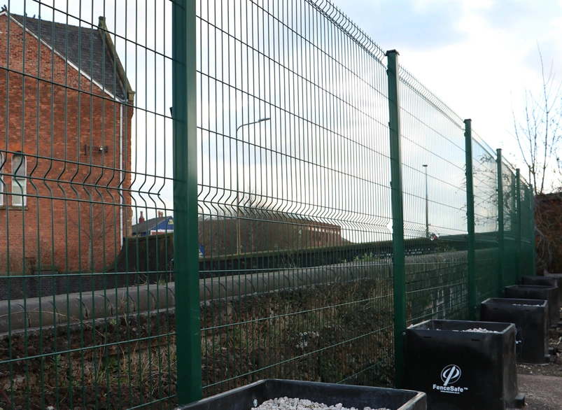 Green welded mesh security fence line with FenceSafe ballast blocks along a roadside