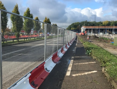 Temporary roadworks safety fencing and red and white bull barriers along a roadside footpath